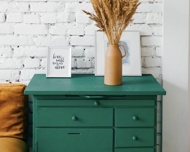 green chest of drawers against a white brick wall